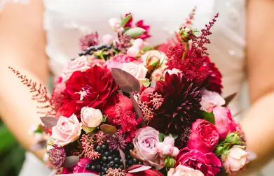 Close-up of a woman's hands delicately holding a lush wedding flower bouquet, featuring a mix of roses, lilies, and greenery for a romantic touch.