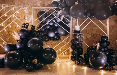 Stylish event decor featuring a cluster of inflated black balloons artfully arranged against a shimmering gold backdrop for a luxurious ambiance.